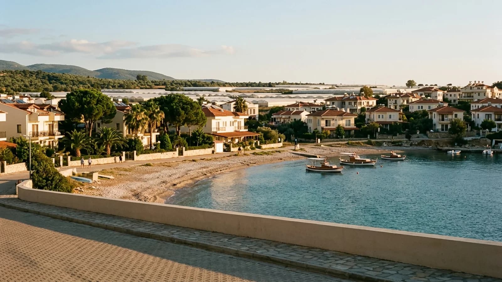 Baai en kiezelstrand van Mavikent Een kleine baai bij Mavikent met kiezelstrand, vakantiehuizen en kassen op het vlakke land erachter.